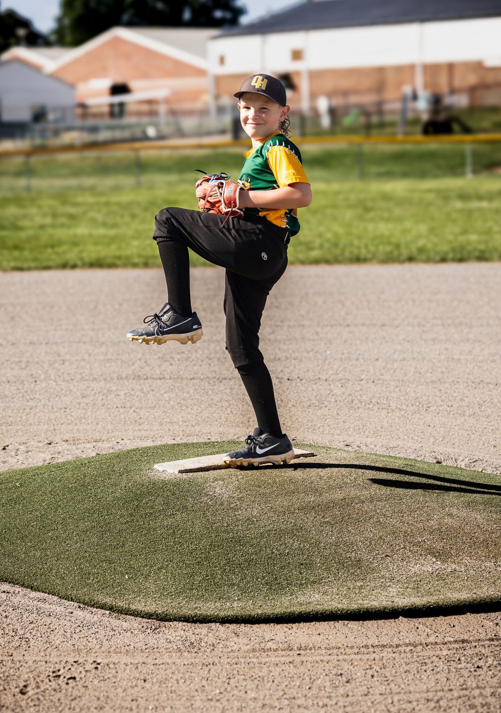Young pitcher in mid-windup motion on baseball mound wearing yellow and black uniform.