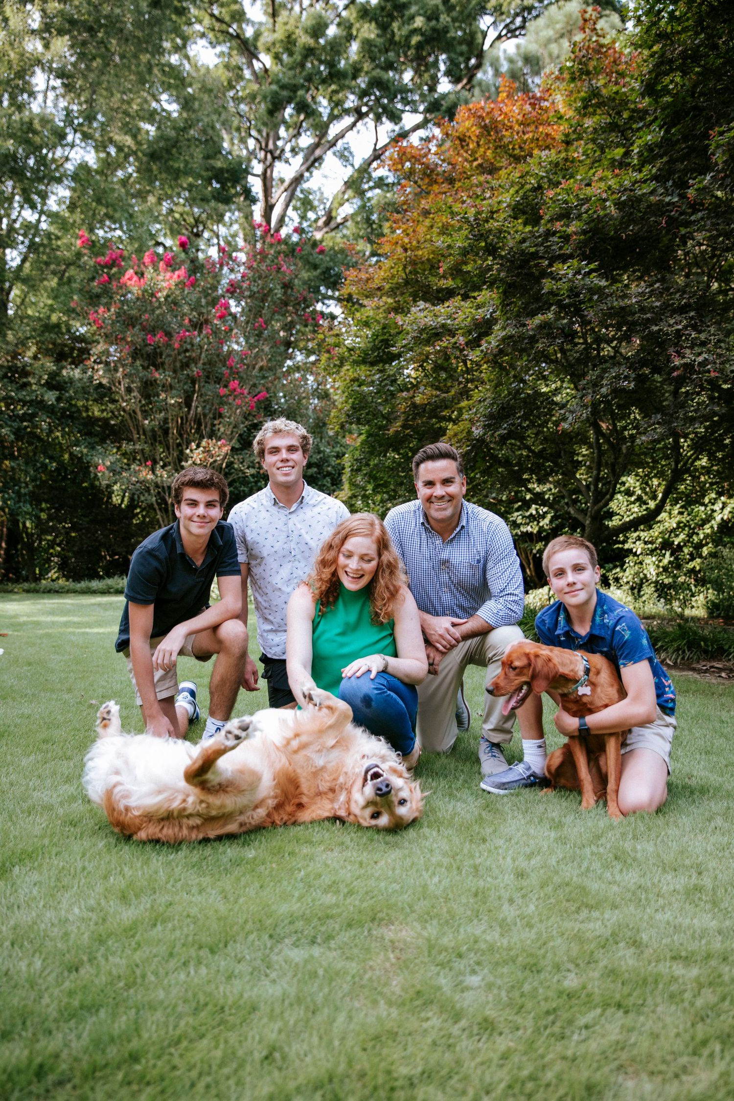 A group gathered on a lush green lawn with a happy golden retriever enjoying the sunny day.