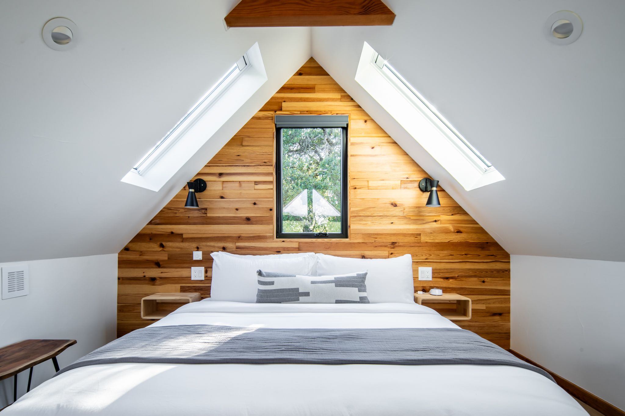 Cozy attic bedroom with wooden accent wall, skylights, and minimalist decor.