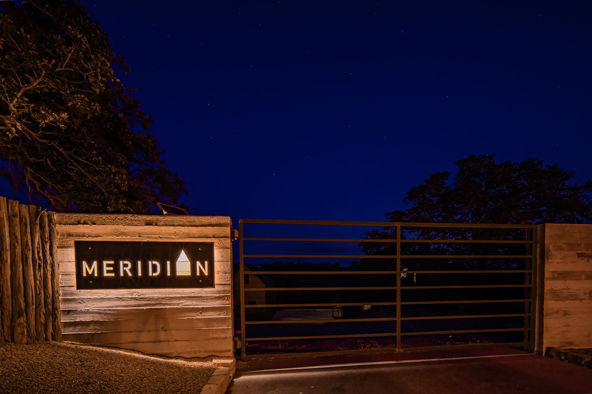 Illuminated entrance gate with 'Meridian' sign at night against dark blue sky.