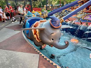 Flying Dumbo ride at Disney theme park with colorful elephants soaring above water features.