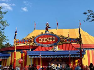 Colorful yellow and red Dumbo circus tent attraction at Disney theme park with flags under blue sky.