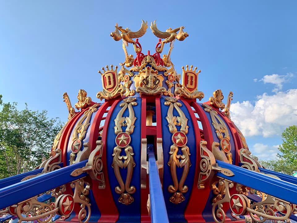 Ornate red, blue and gold fairytale-themed circus tent or carnival canopy top against blue sky with decorative details.