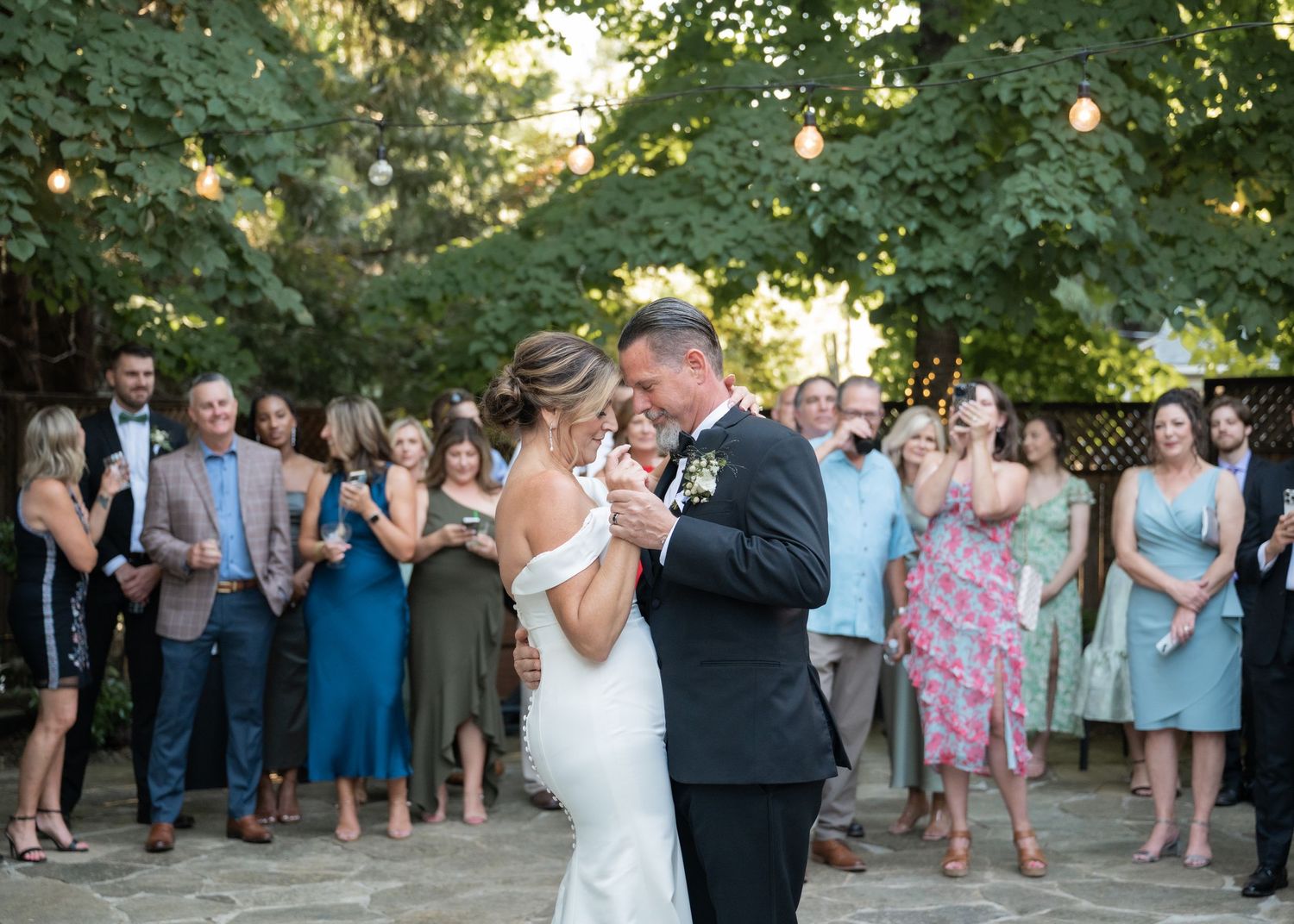 A bride and groom on their wedding day sharing a private moment during their first dance while friends, family, and wedding guests look on