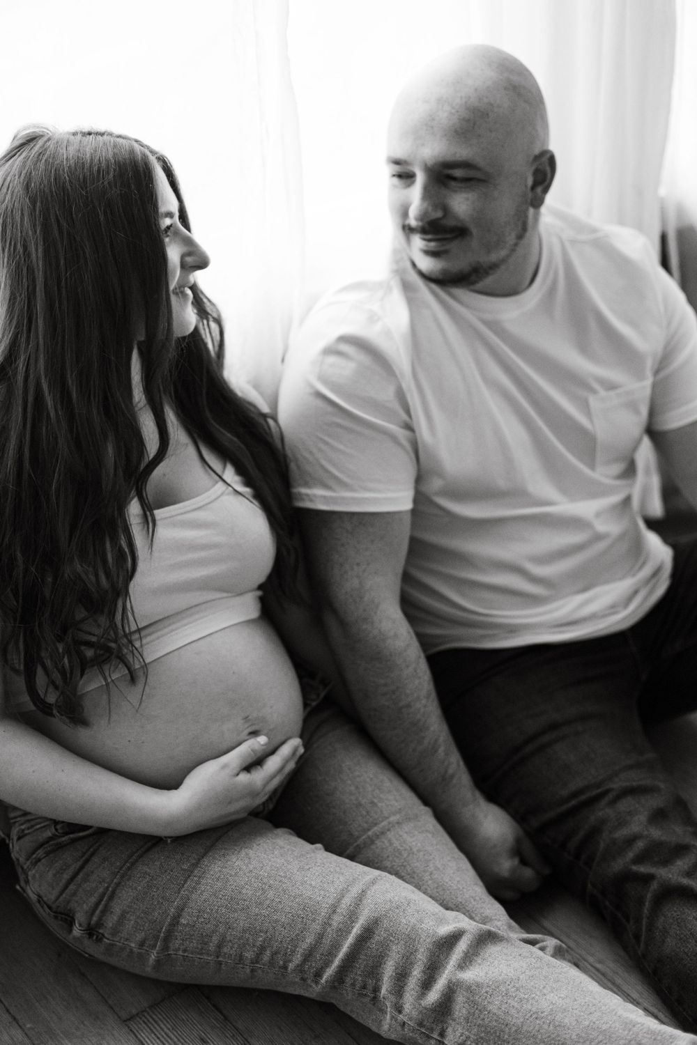 Black and white intimate maternity photo of couple sharing tender moment while sitting together at home.
