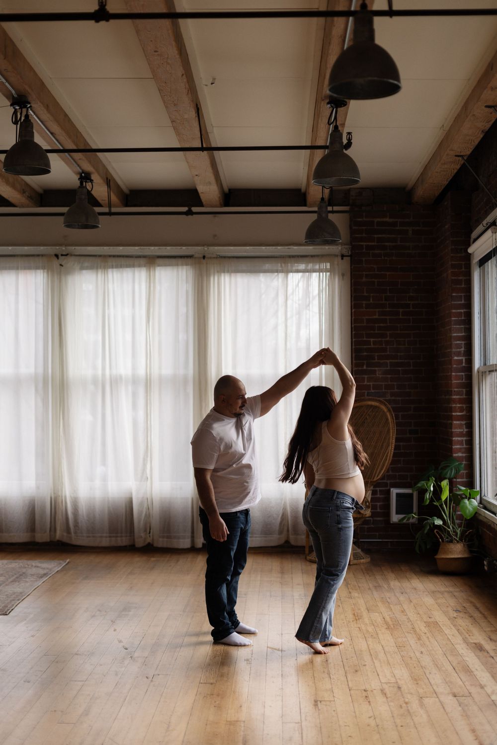 A couple practices dancing together in a spacious industrial studio with exposed brick walls and natural light.