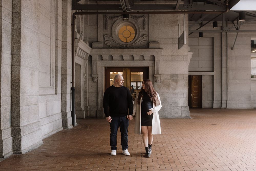 Two people stand together in an elegant corridor with stone columns and terracotta floor tiles.