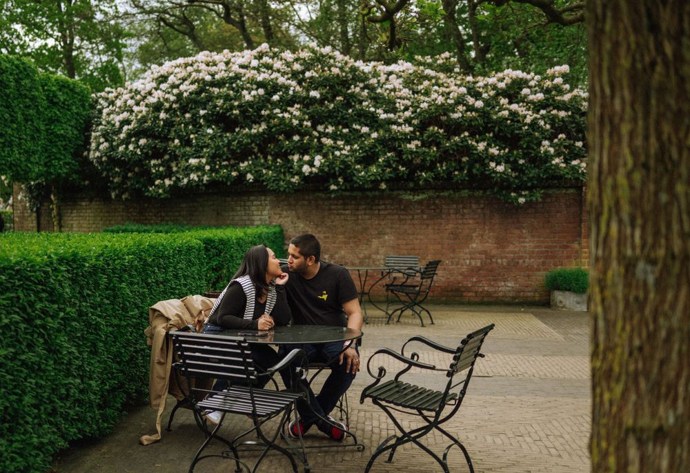 Intimate moment shared on park bench surrounded by flowering bushes and manicured hedges.