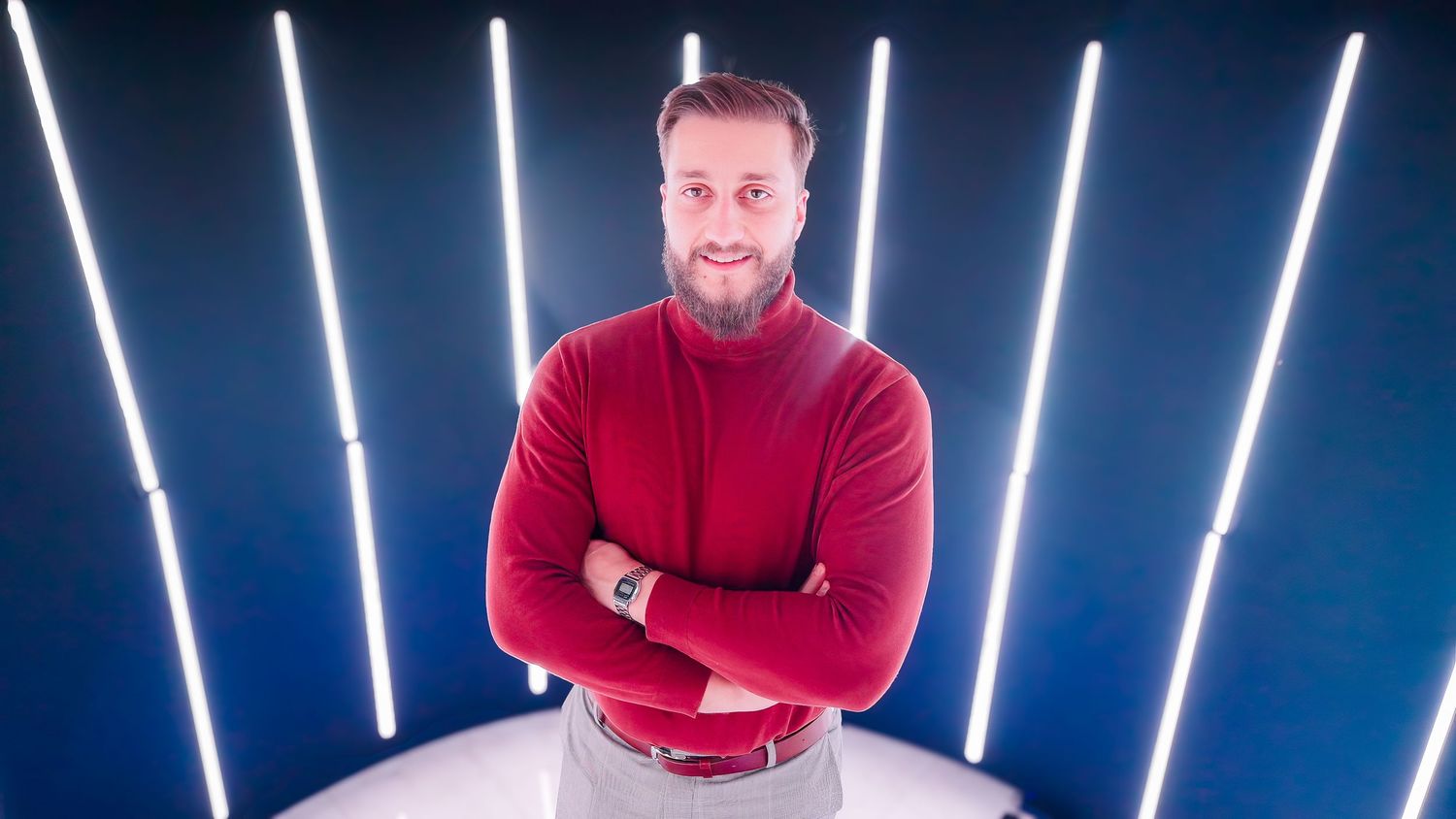 Person in a red sweater standing with crossed arms against blue background with vertical white light bars.