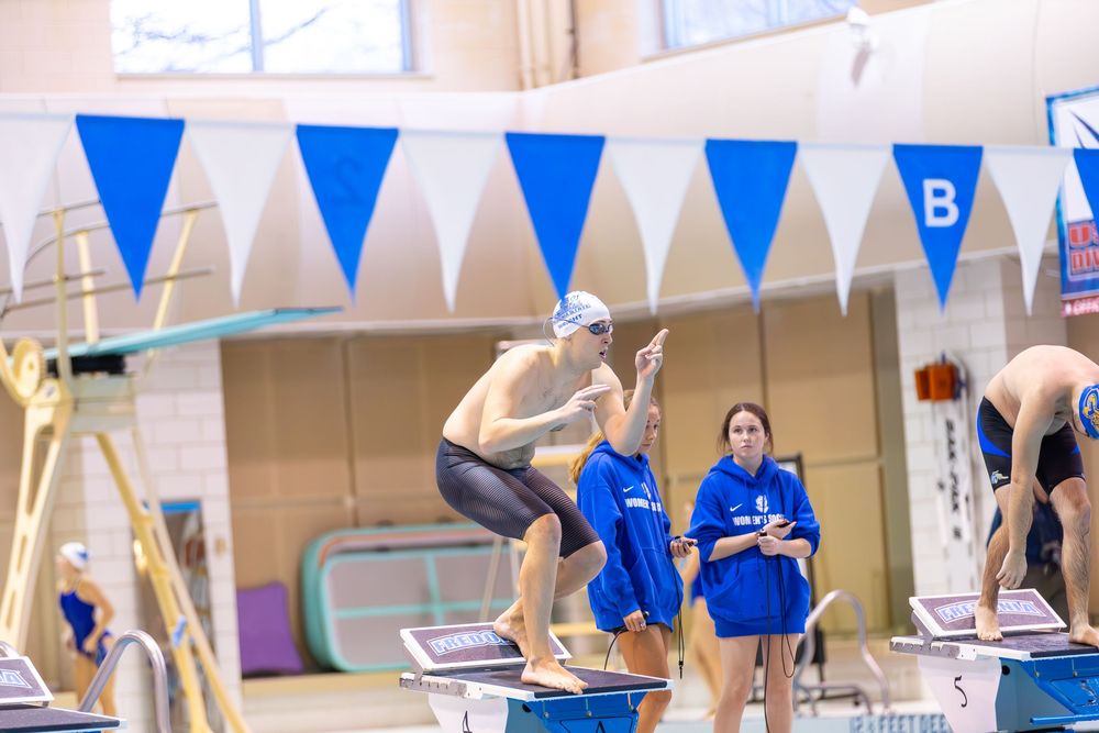 Blue and white triangular flags hang above an indoor swimming pool during a competitive event.