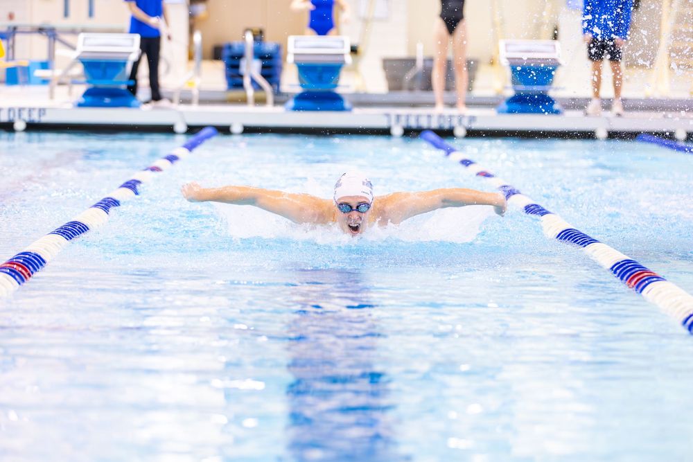 Swimmer performing butterfly stroke in competition pool with lane lines and blue water.
