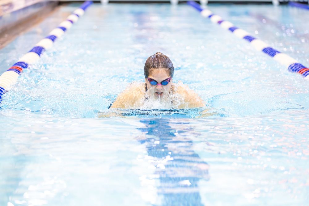 Competitive swimmer performs breaststroke technique in a pool lane during race or practice session.