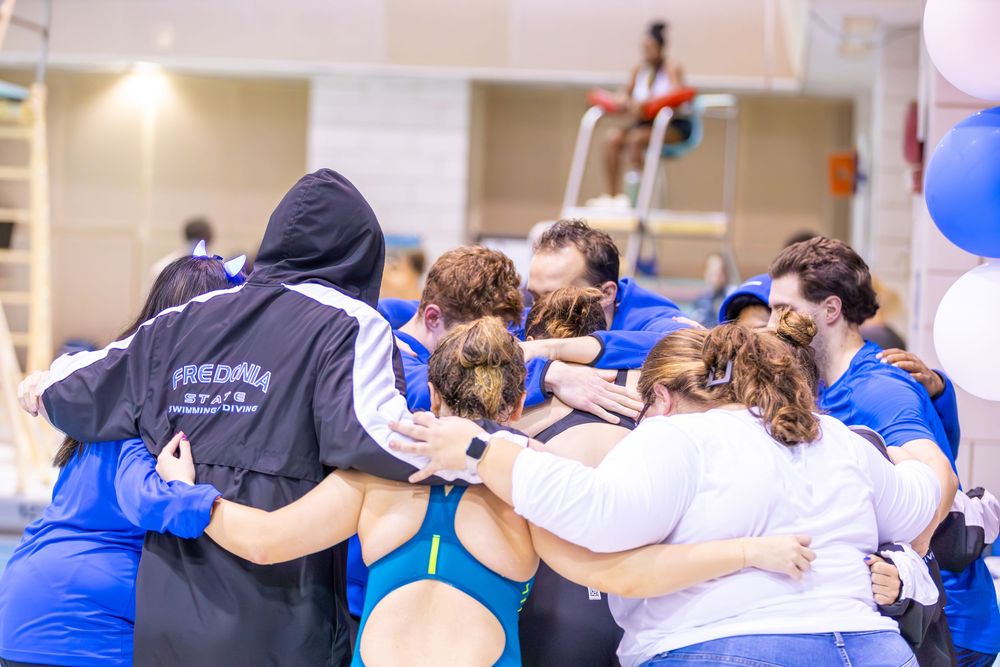Team members stand in a line with arms linked during a swimming competition event.
