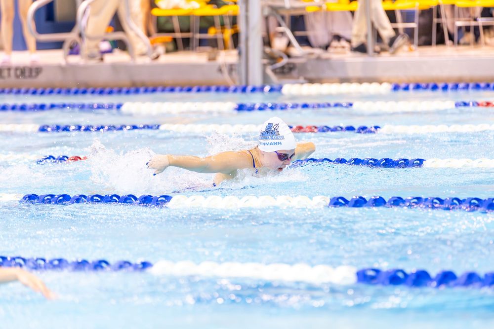 Competitive swimmers race in multiple lanes during a swimming meet at an indoor pool.