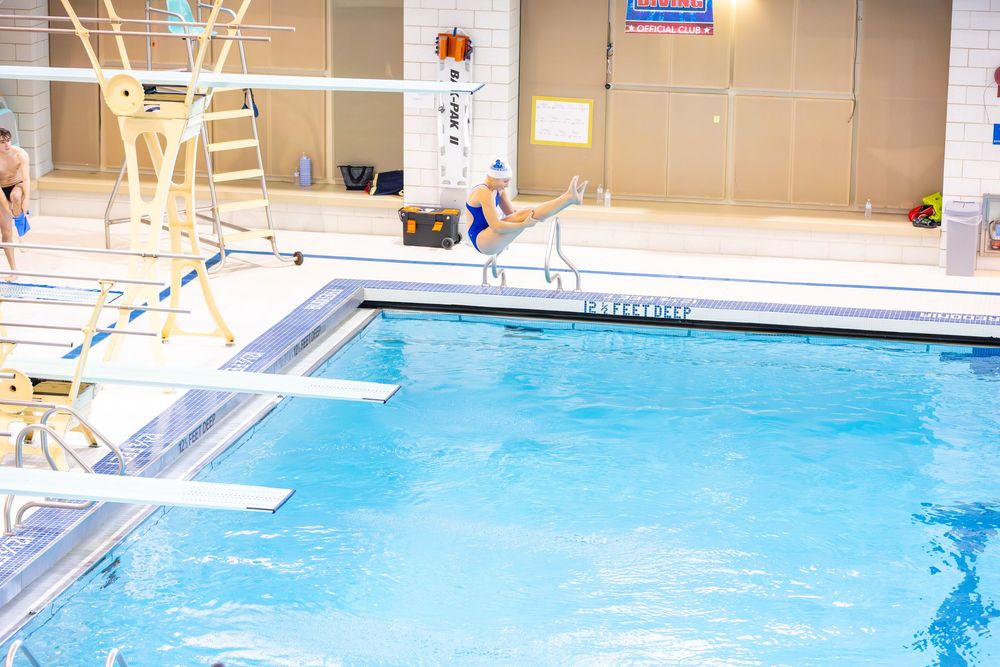 Indoor swimming pool with diving boards and bright blue water illuminated by natural light through windows.