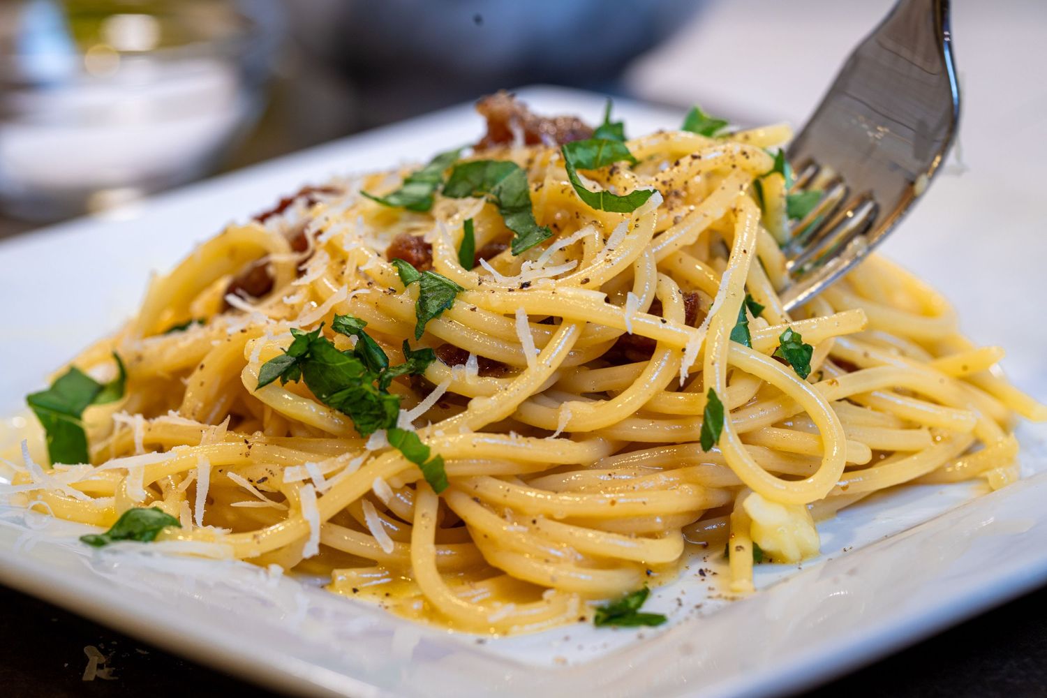 Fresh carbonara garnished with basil and parmesan cheese on a white plate.