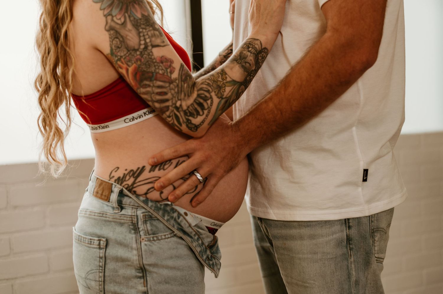 A close-up photo showing tattooed hands cradling a pregnant belly.