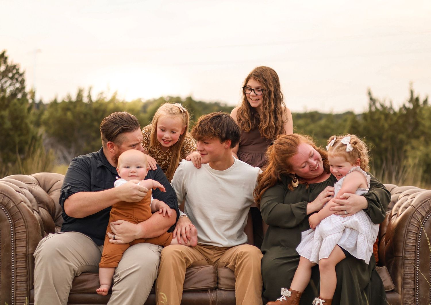 A candid family moment of laughter and joy on a wicker outdoor sofa at sunset.