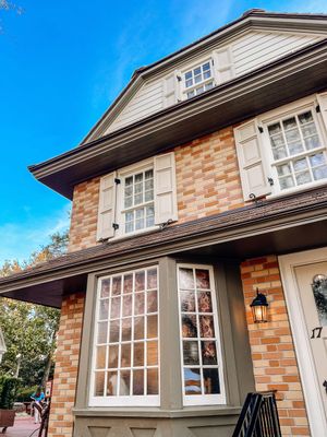 An architectural detail of a colonial style brick house with large windows, gray trim, and a black lamp fixture.