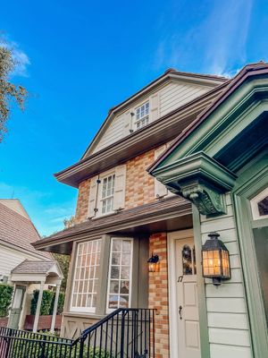 Architectural details of elegant brick and sage green cottages with lantern-style lights and ornate trim under blue skies.
