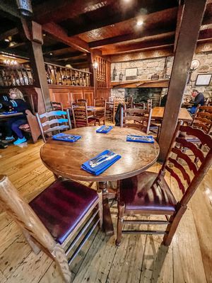 Rustic restaurant interior with wooden table set with blue placemats, ladder-back chairs and exposed beam ceiling.