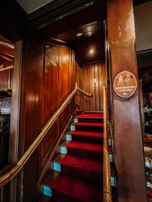Elegant wooden staircase with red carpet and brass handrails in a restaurant interior features warm lighting and rich paneling.
