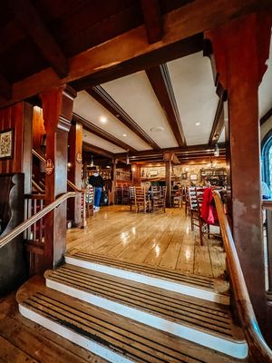 Interior view of a rustic pub or restaurant with wooden steps, exposed beams, and warm lighting creating a cozy atmosphere.