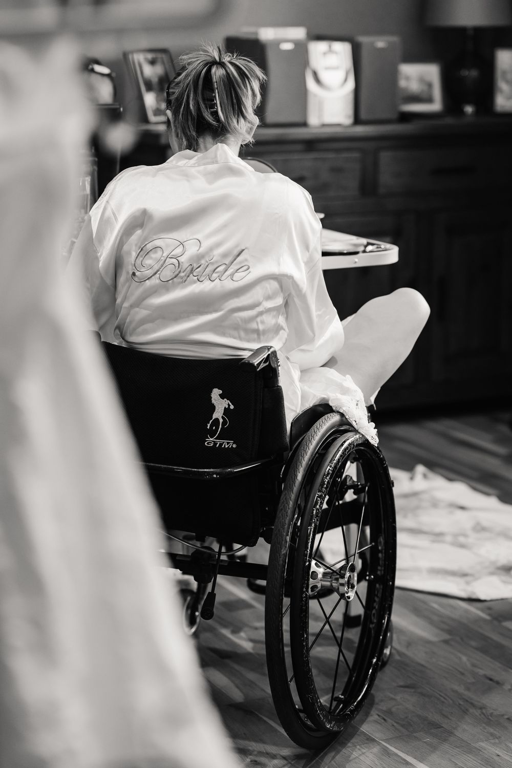 Black and white photo of a bride in a wheelchair wearing a white Bride robe, preparing for her wedding day.