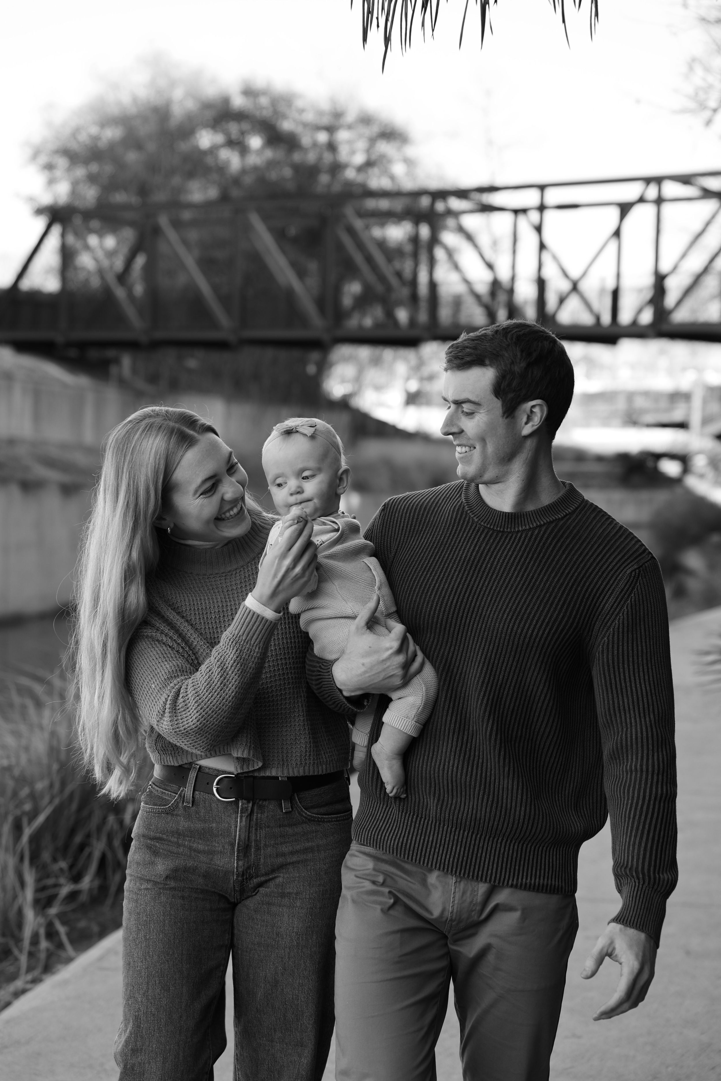 Black and white photo of a couple walking with their baby on a path on the San Antonio River Walk.