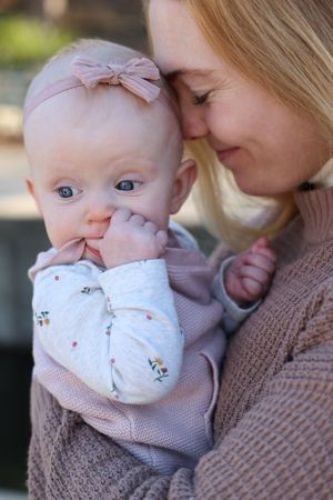 A tender moment between parent and baby wearing a pink bow headband and floral onesie.