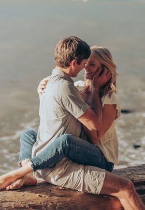 A tender romantic moment captured between two people sitting on driftwood by the sea.