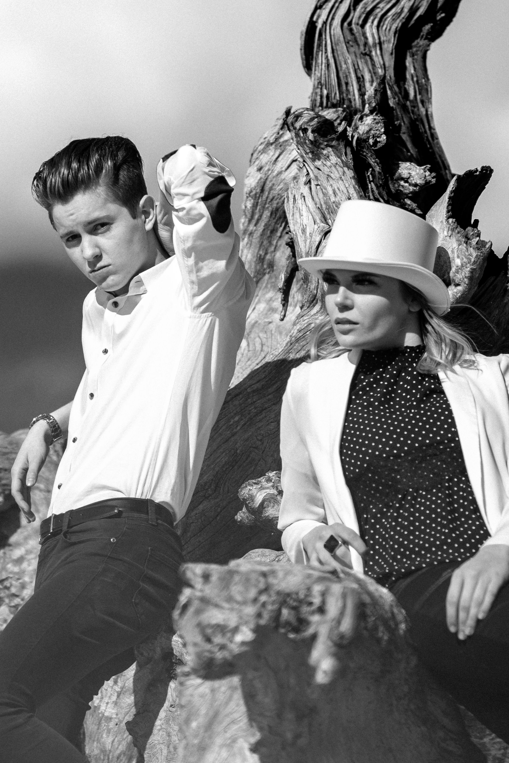 Black and white fashion photo with two models posed dramatically on weathered wood.