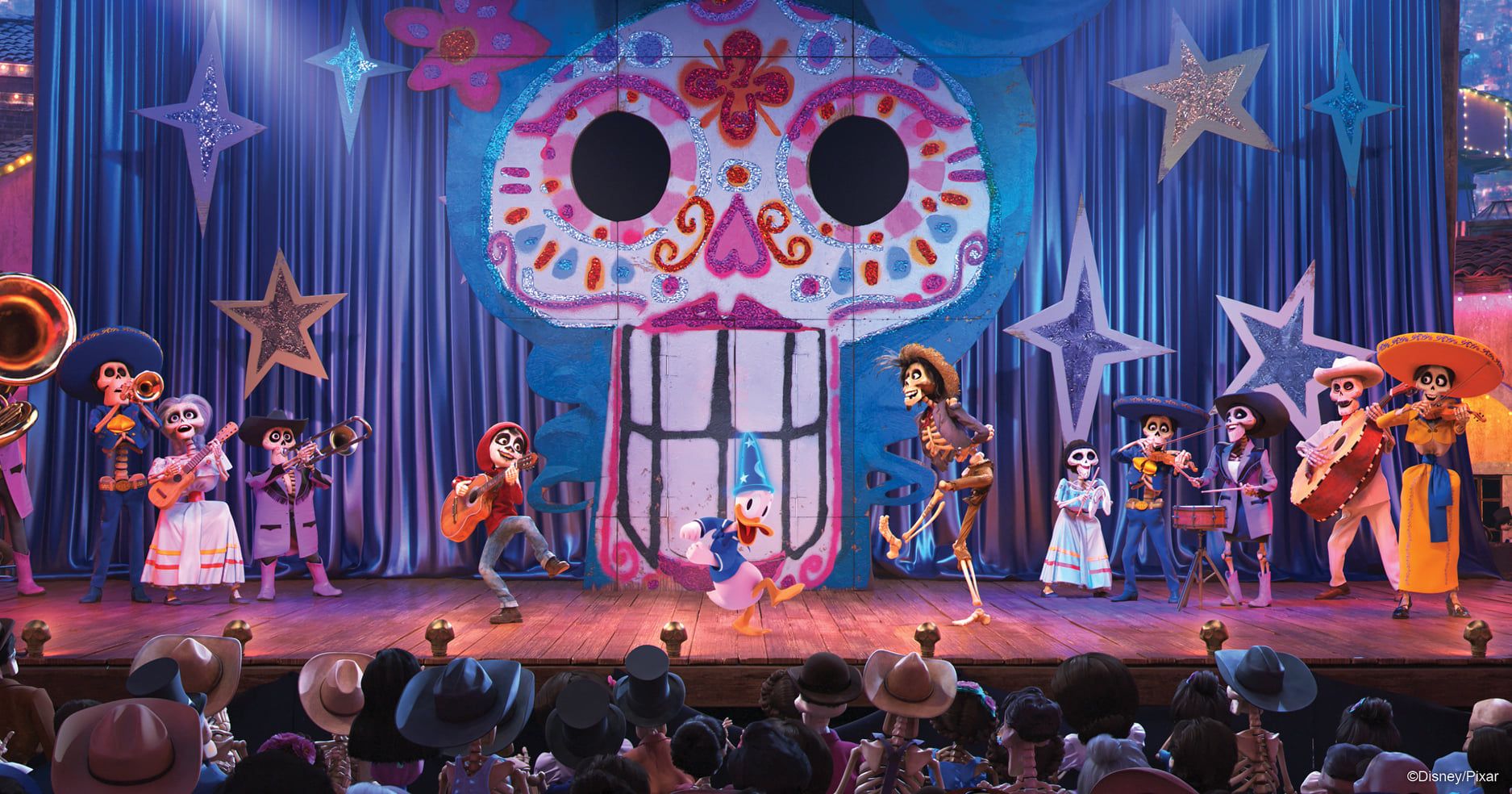A colorful musical theater stage performance with actors in costumes performing under bright lights and decorative set pieces.