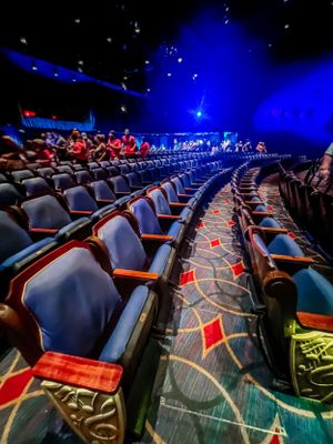 Curved rows of plush theater seats with geometric carpet patterns under dramatic blue lighting in an entertainment venue.
