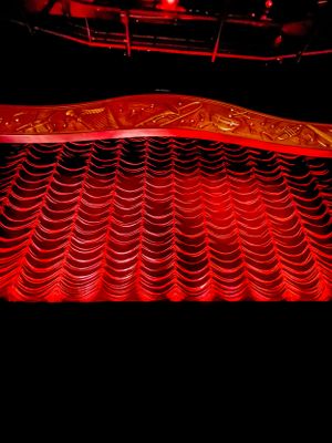 Red theater curtain with ornate scalloped pattern illuminated by dramatic lighting in a dark performance space.