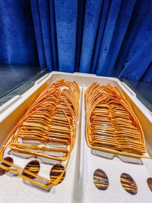 Several rows of neatly arranged orange sunglasses displayed on a white surface against a deep blue curtain backdrop.