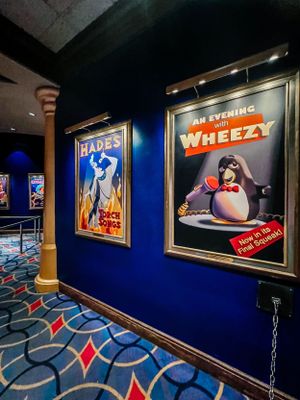 A dimly lit hallway with blue walls features illuminated theater posters and decorative carpet with geometric patterns.