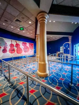 Interior view of a modern exhibition space with geometric floor patterns in blue and red, featuring illuminated columns and walls.