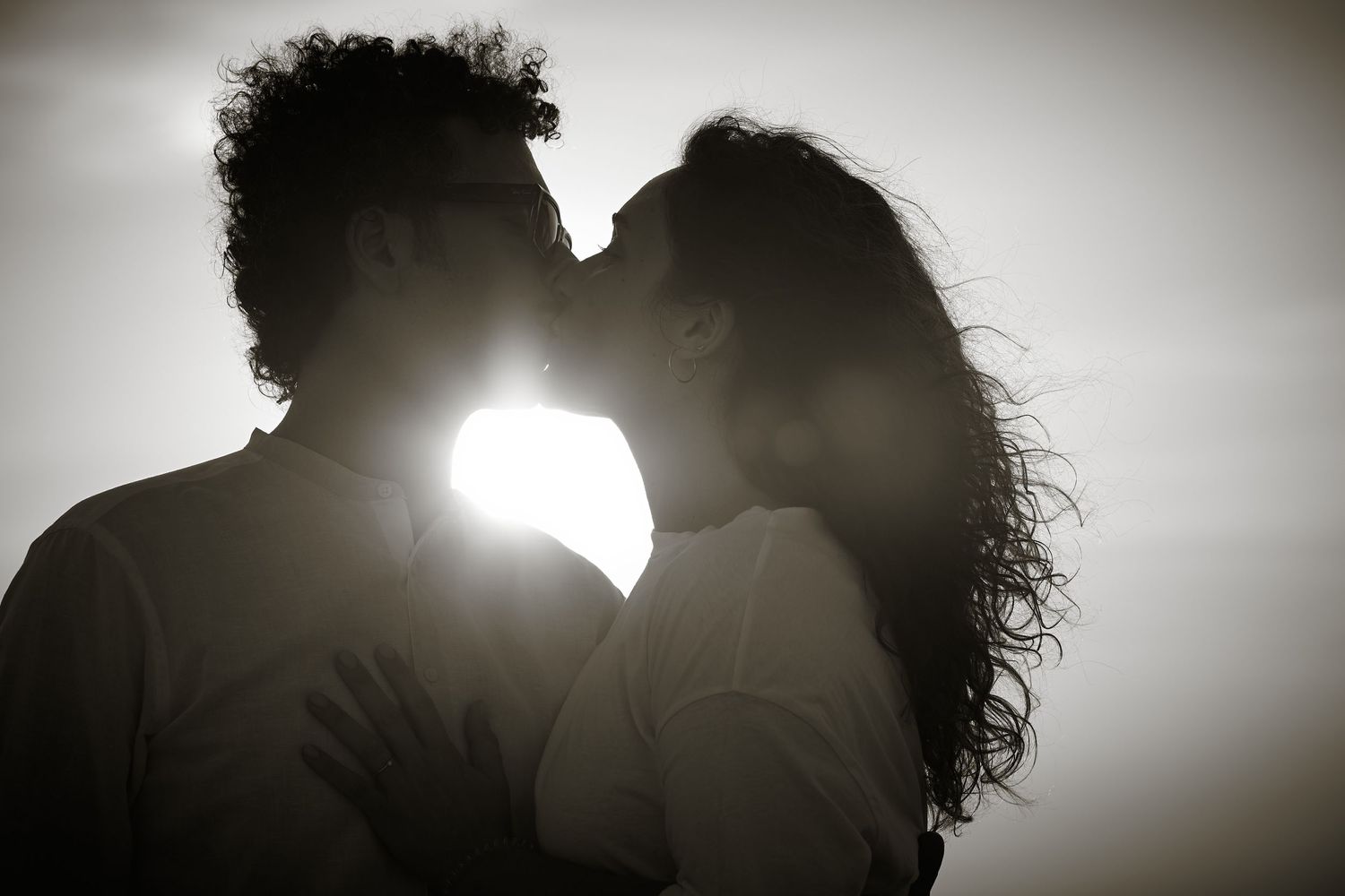 Silhouetted couple with curly hair sharing an intimate moment backlit by bright sunlight creating a romantic glow.