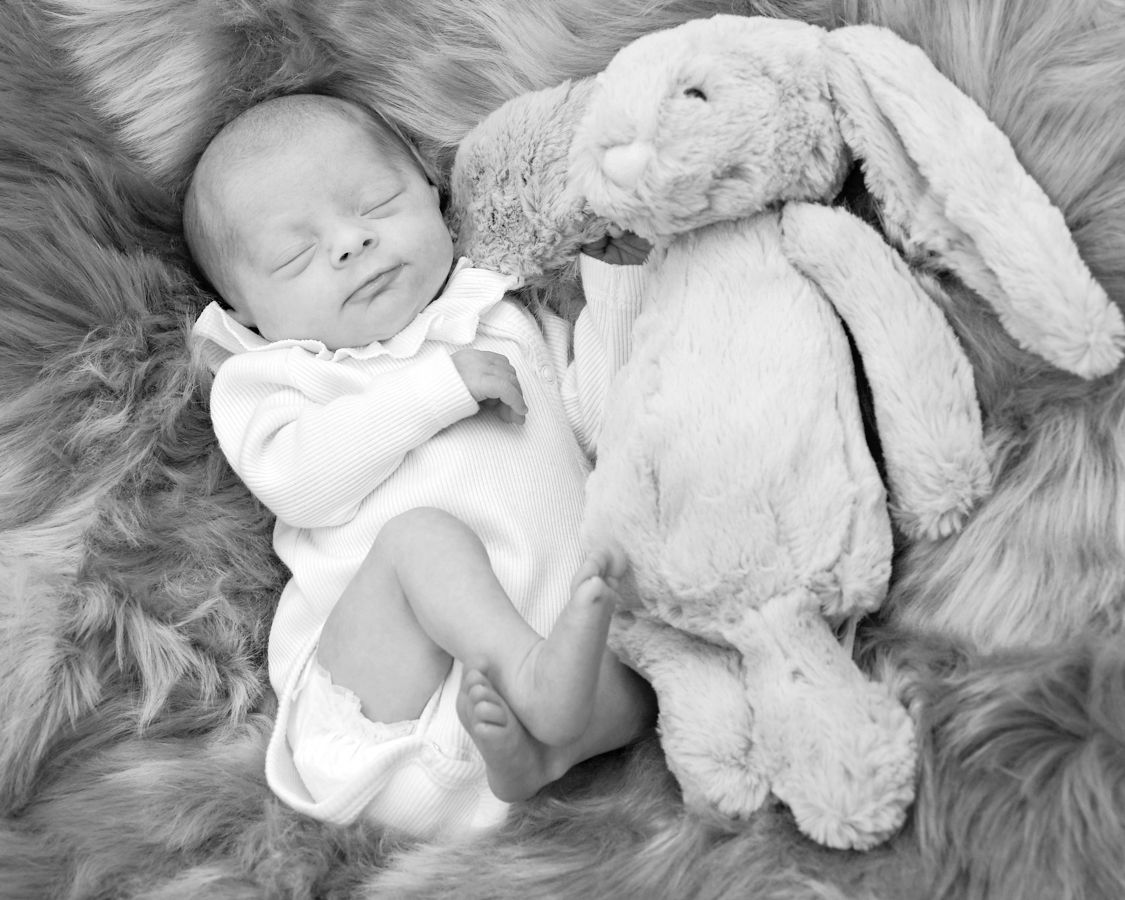 A peaceful newborn baby sleeps beside a soft stuffed rabbit, beautifully photographed by Abigail's Studio.