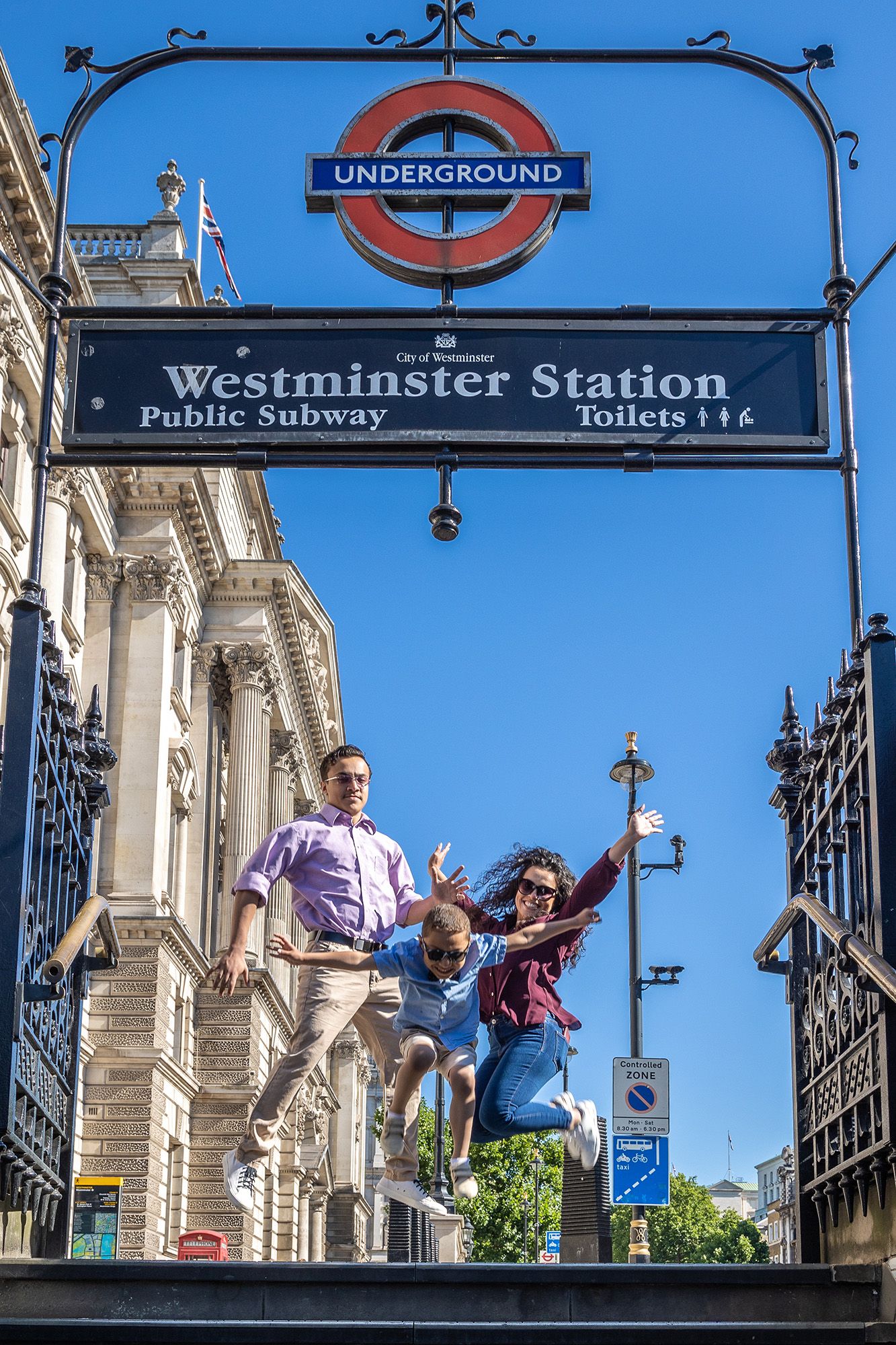 People jumping joyfully outside the Westminster Underground station entrance in London with iconic roundel sign and architecture.