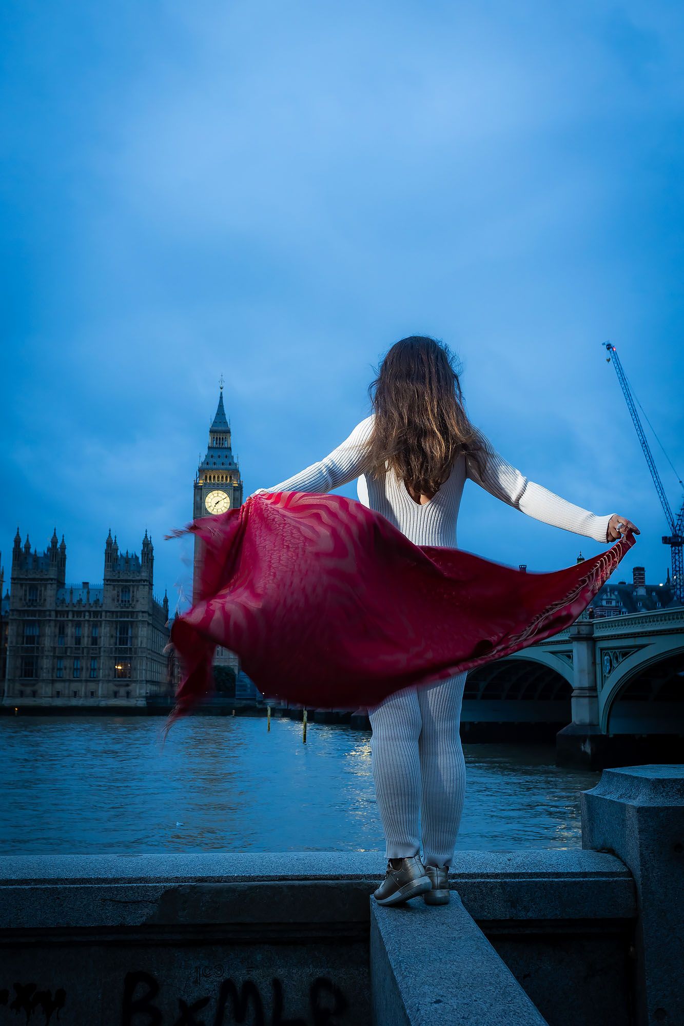 Dancer in a red skirt poses against London's Big Ben and Westminster Bridge during blue hour.