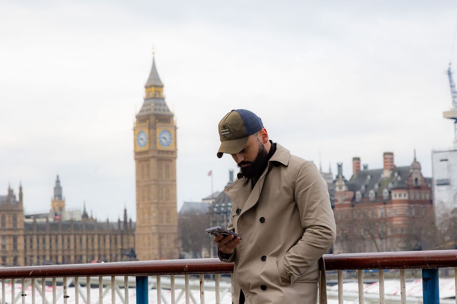 A traveler in a beige coat stands on a bridge near Big Ben and the Houses of Parliament in London.