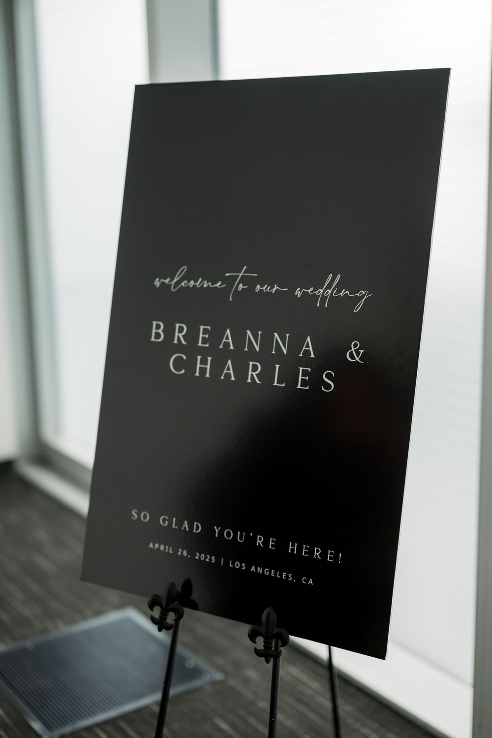 Modern black wedding welcome sign for Breanna and Charles on an easel against a window.