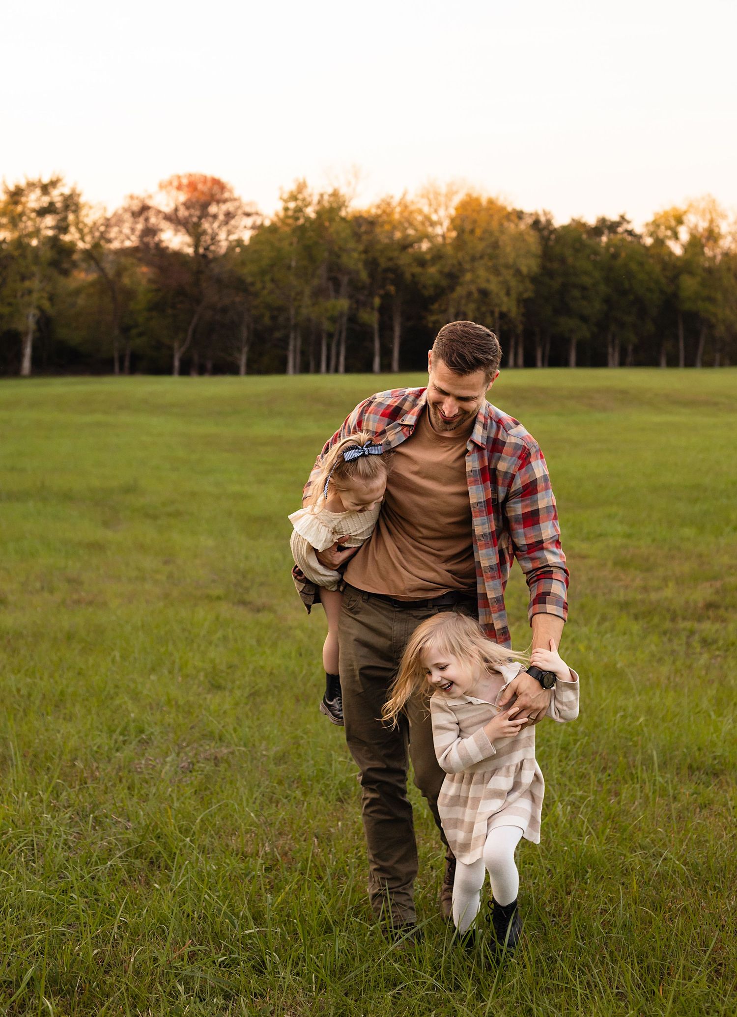 Fun dad running and playing with small daughters in a field during a fall family photography session in Charlottesville, Virginia.