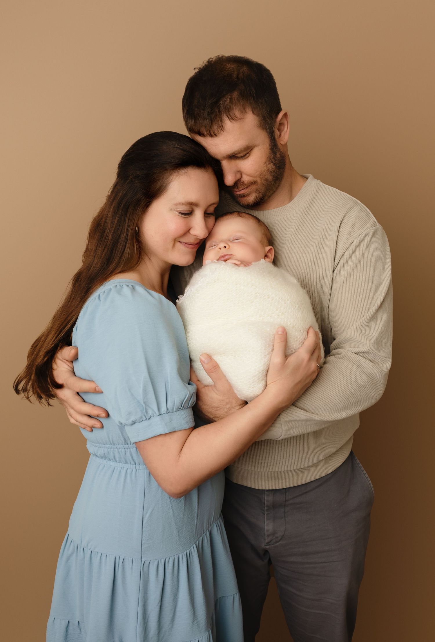 Charlottesville newborn photographer, baby, family, mom in blue and dad in beige sweater holding baby girl wrapped in white.