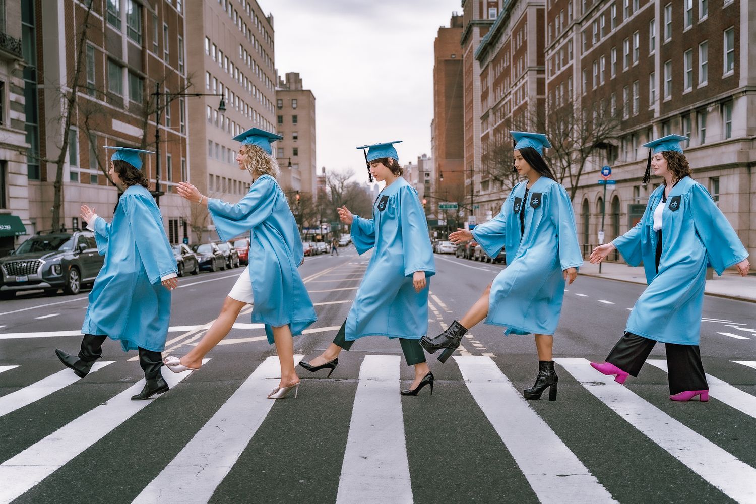 Five graduates in light blue gowns recreate Abbey Road crossing photo.
