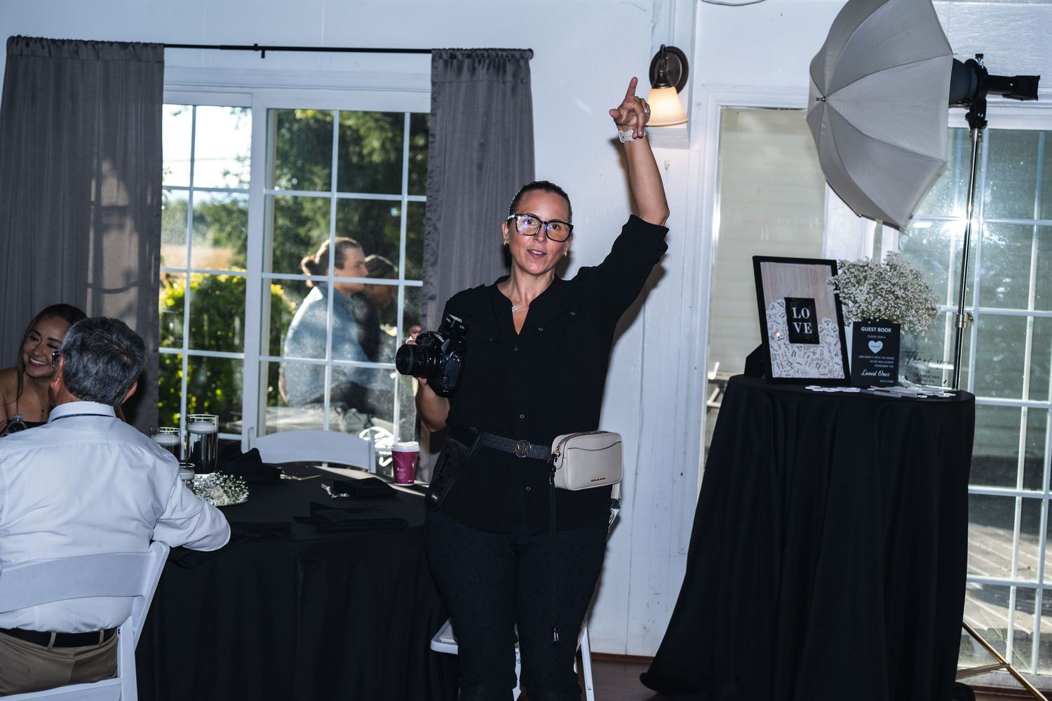 A person in black clothing raises their arms in celebration during an indoor event with lighting equipment visible.
