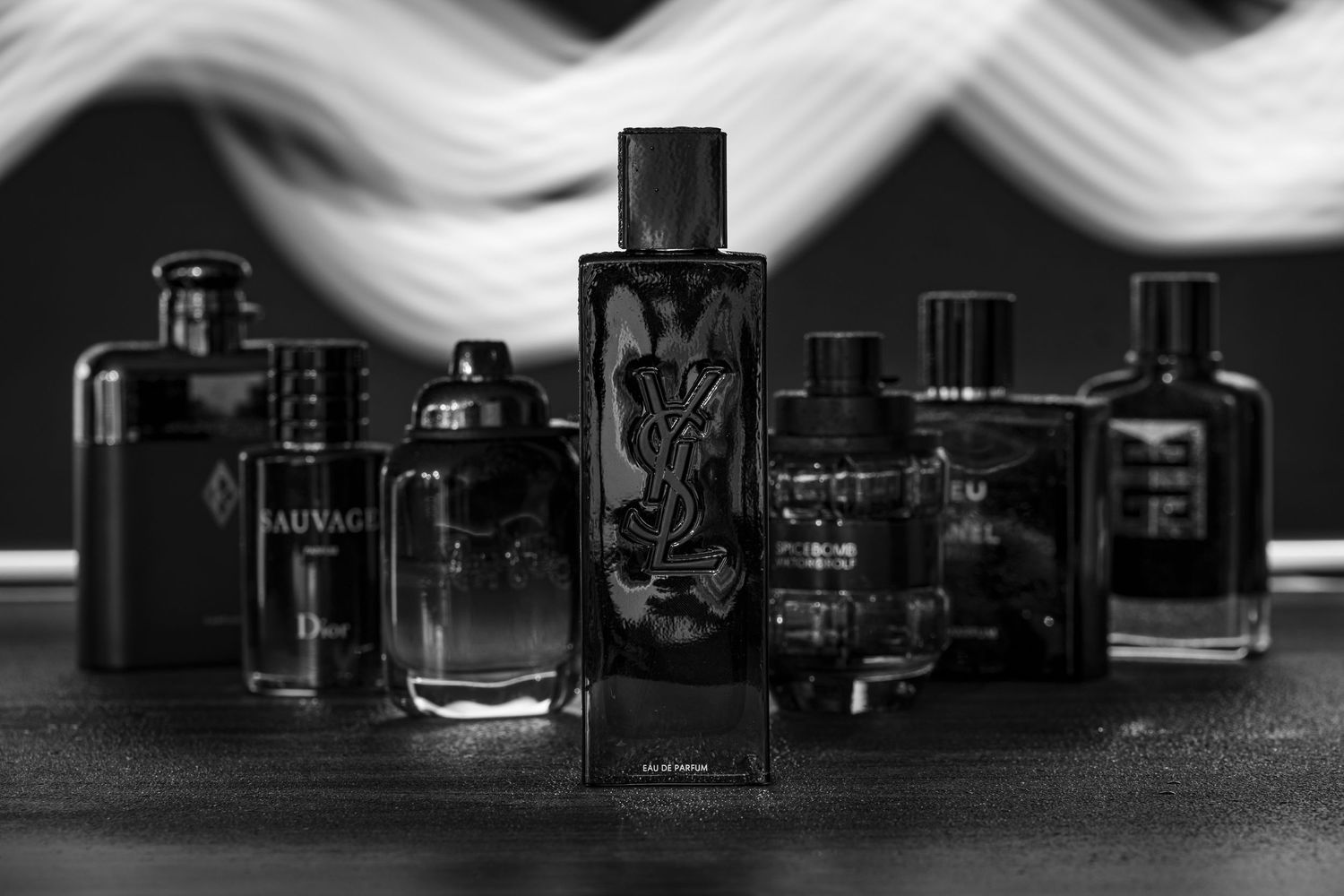 Black cologne bottle in focus with misty vapour and water droplets, surrounded by other dark bottles in a dramatic setup.