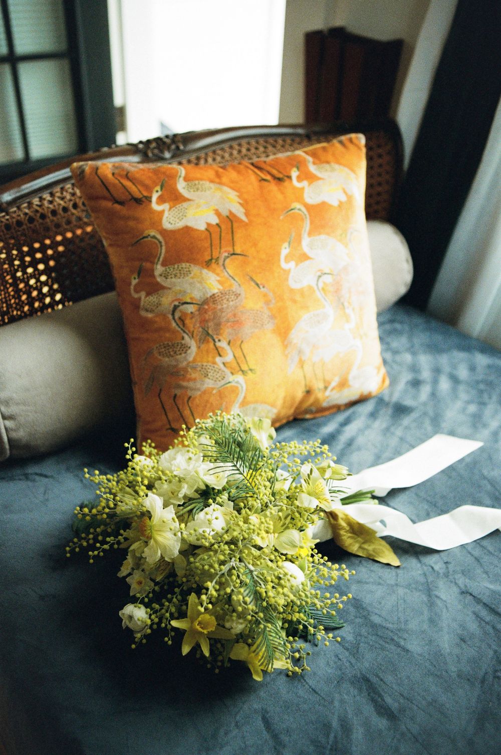 Orange decorative pillows and yellow floral arrangements rest on dark linens in a wedding setting.